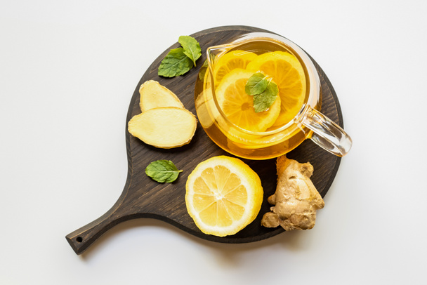 vue du dessus du thé chaud en théière servi sur une planche de bois avec racine de gingembre, citron et menthe sur fond blanc
 - Photo, image