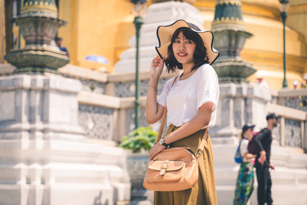 Portrait of Asian woman wearing a hat traveling in Phra Kaew temple in Bangkok, Thailand. - Fotó, kép
