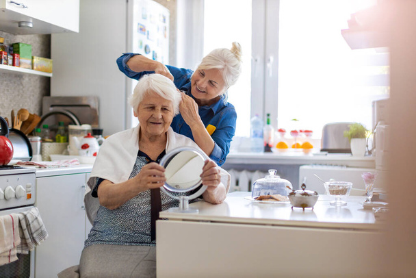 Woman cutting her elderly mother's hair at home - Fotoğraf, Görsel