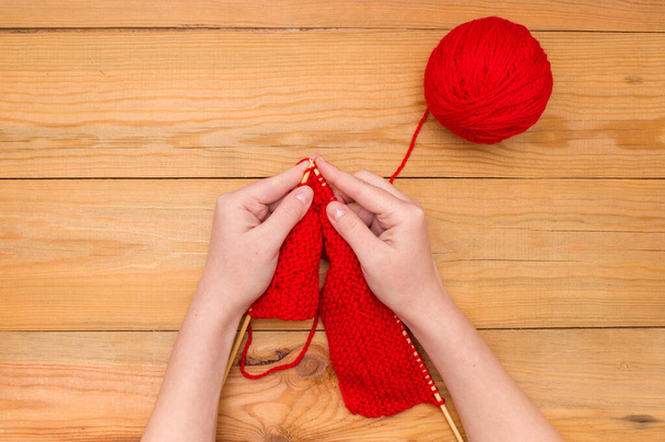 Mãos de mulher com agulhas de tricô e uma bola vermelha de fio em um fundo de madeira
. - Foto, Imagem