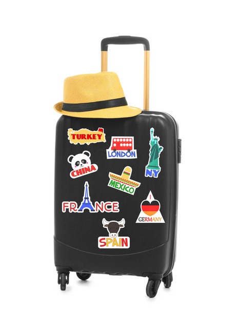 Modern suitcase with travel stickers and hat on white background - 写真・画像