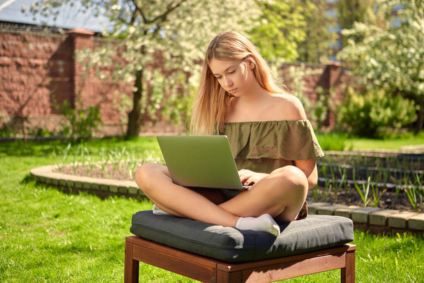 Creative young girl blogger working on a laptop on content sitting in the backyard of a house in the garden on a lawn. - Foto, Bild