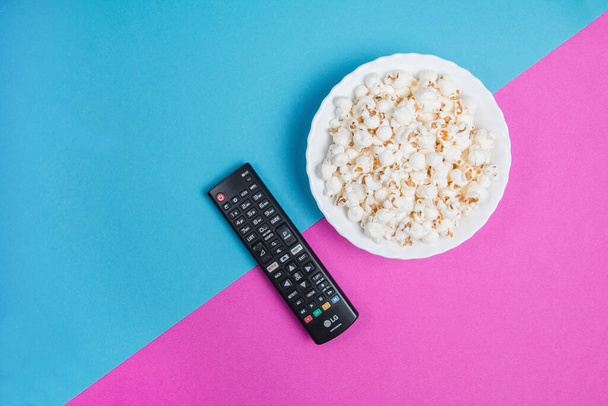 Biała miska popcornu na niebiesko-fioletowym tle z czarnym pilotem TV - Zdjęcie, obraz