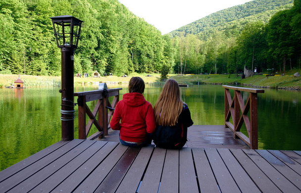 Boy and girl sitting on pier at lake in mountains of Carpathians - Photo, Image