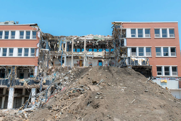 A partially demolished building. Much of the center of the building is missing, and there is a large pile of dirt in front. Lots of debris and hanging wires. Bright sunny day. - Fotografie, Obrázek
