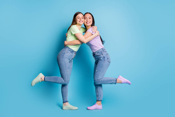 Full size profile photo of cheerful two lesbians couple overjoyed hugging young students best friends buddies eyes closed wear casual t-shirts jeans footwear isolated blue color background - Фото, зображення