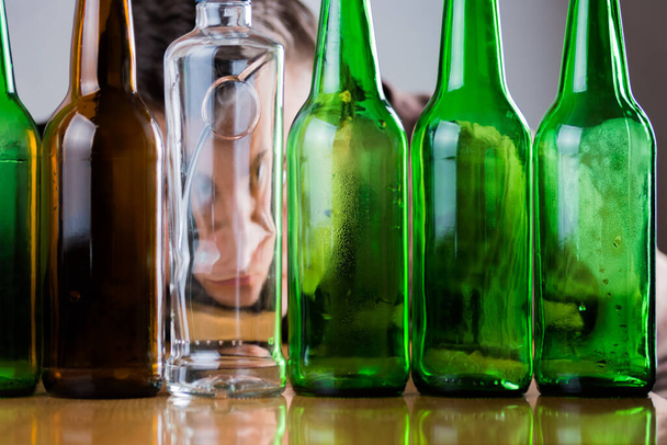 Smutny młody człowiek za zielonymi i brązowymi butelkami szkła. Zwalczanie problemu uzależnienia od alkoholu abstrakcyjna koncepcja. - Zdjęcie, obraz