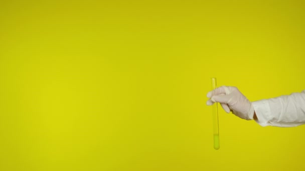 Ręka w rękawicy ochronnej pokazuje szklaną rurkę z żółtą substancją - Materiał filmowy, wideo