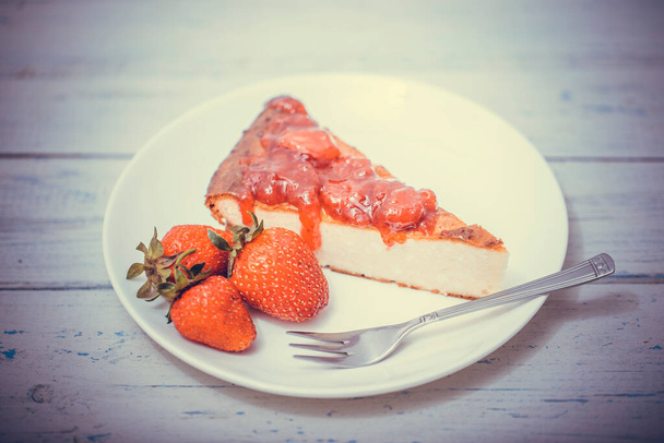 Brownie-Käsekuchen mit Erdbeeren perfekt auf einem Teller auf weißem Holztisch angeordnet. - Foto, Bild