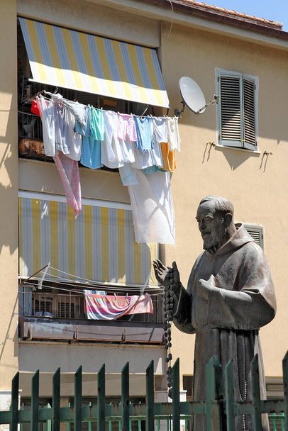 Taranto, Puglia, İtalya 'da popüler bir mahallede balkonları ve kıyafetleri asılı Peder Pio heykeli. - Fotoğraf, Görsel