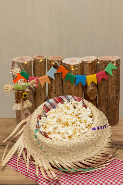 Palomitas de maíz servidas en un sombrero de paja con decoración de fiesta de junio en el fondo. Festa Junina: Típica fiesta brasileña de junio
. - Foto, Imagen
