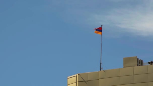 Ormiańska flaga macha na wysokim dachu budynku przed błękitnym niebem w słoneczny dzień w Erywaniu, Armenia - Materiał filmowy, wideo