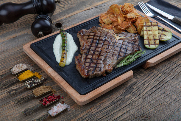 Barbecued t-bone steak seasoned with fresh herbs and marinade served with a cutting board in a steakhouse. Delicious restaurant food - Фото, изображение