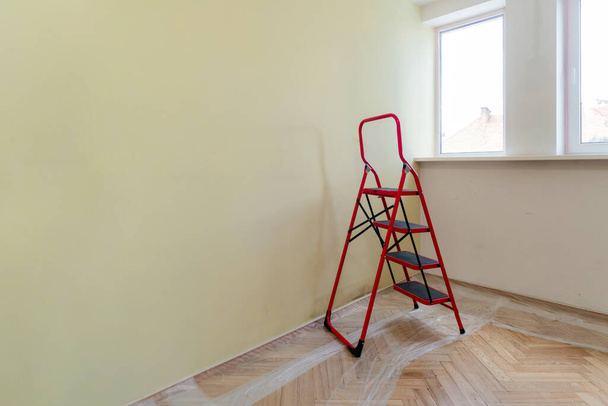 Habitación vacía con una escalera antes de pintar las paredes. Protección de celofán en suelo de madera. Renovación del hogar. Nadie.
 - Foto, Imagen