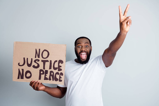 No justice no peace. Photo of cheerful dark skin afroamerican protester hold placard against black citizens lawlessness concept show v-sign positive attitude isolated grey color background - 写真・画像