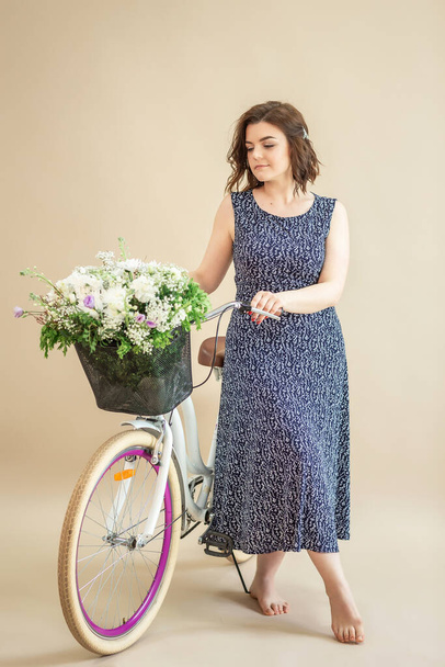 Woman riding a bike with flowers on beige background. - Фото, изображение