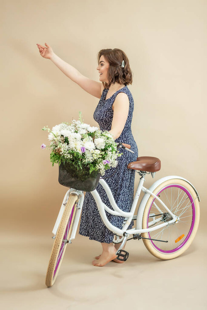 Happy young girl riding bicycle with flowers. on beige background. - Foto, Imagen