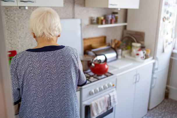 Οπίσθια όψη ηλικιωμένης γυναίκας στην κουζίνα της - Φωτογραφία, εικόνα