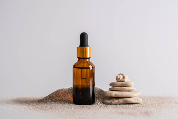 Glass brown bottle of serum with a pipette for skin care is on the sand with stones and shells. Cosmetics with marine components. The concept of health and beauty. minimalism, copy space - Foto, immagini