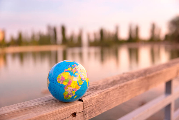 Malá světová koule umístěná na dřevěném plotě velkého jezera. Cestovní koncepce a péče o planetu. - Fotografie, Obrázek