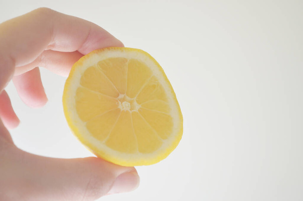 Лимон крупным планом, разрезанный пополам одной рукой.
 - Фото, изображение