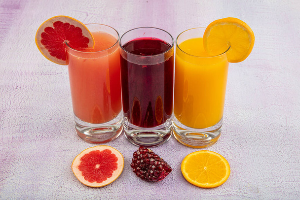 白い木の背景に爽やかな柑橘系のカクテルとグラス。ザクロジュース、オレンジジュース、グレープフルーツジュースの抗酸化ジュース. - 写真・画像
