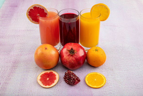 Vajilla con refrescante cóctel de frutas cítricas sobre fondo de madera blanca. Jugos antioxidantes de jugo de granada, zumo de naranja, zumo de pomelo
. - Foto, Imagen