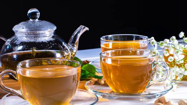 Чайник и кружки с зеленым чаем, орехи кешью, зеленые листья и белые цветы гипсофилы. Дневной чай, домашний. Восточная, уютная, приготовленная, отварная, травяная
 - Фото, изображение