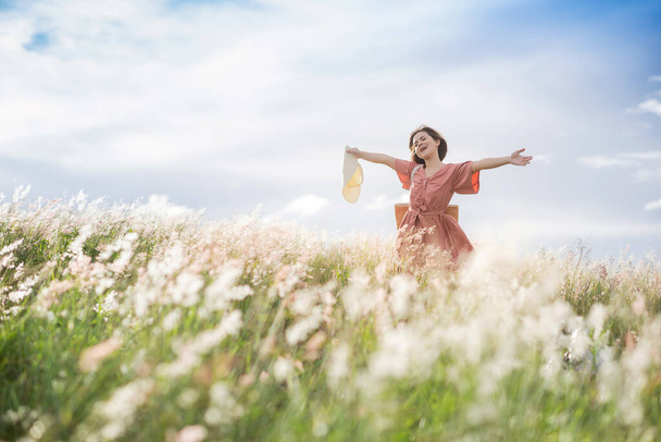 A young Asian girl on a beautiful spring meadow. She wears a pink dress and wide-brimmed hat. - Photo, image