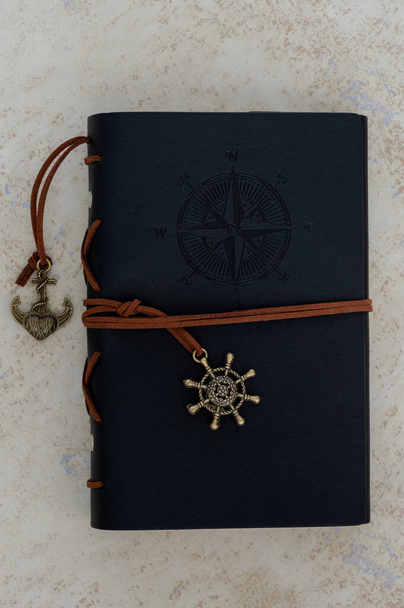 Vintage czarny notatnik z motywem podróży ze złotą kotwicą, sterem statku i drukiem kompasu. - Zdjęcie, obraz