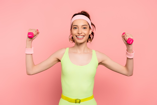 cheerful sportswoman exercising with dumbbells on pink  - Photo, Image
