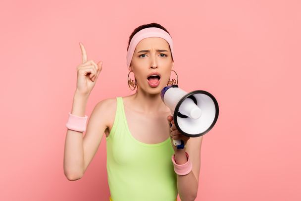 emotionale junge Frau zeigt mit dem Finger und hält Lautsprecher isoliert auf rosa  - Foto, Bild