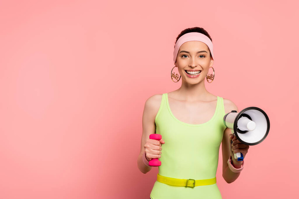 happy sportswoman holding dumbbell and loudspeaker on pink  - Фото, изображение