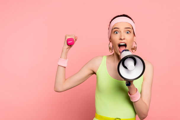emotional sportswoman holding loudspeaker and dumbbell while screaming on pink  - Photo, image