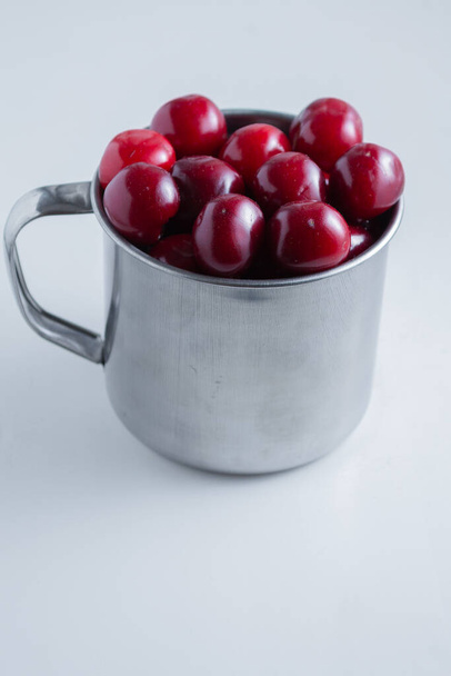 Sweet cherries in a steel mug on a white paper background - Fotoğraf, Görsel