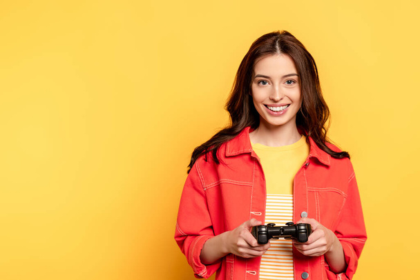 KYIV, UKRAINE - MAY 25, 2020: happy young woman holding joystick and playing video game on yellow  - Foto, immagini