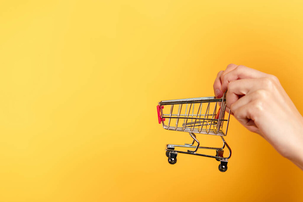 cropped view of woman holding small shopping cart on yellow  - Fotografie, Obrázek