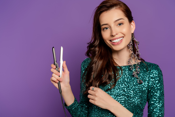 cheerful woman holding small hair straightener isolated on purple - Foto, imagen