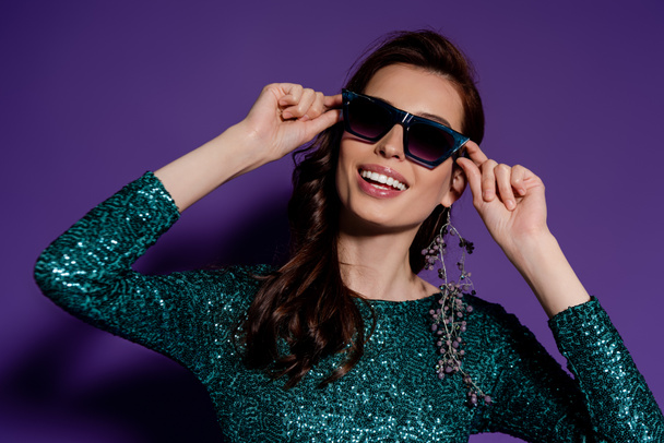 stylish woman touching sunglasses and smiling on purple  - Fotoğraf, Görsel