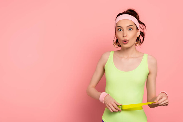 surprised woman with headband touching belt on bodysuit on pink  - Photo, image
