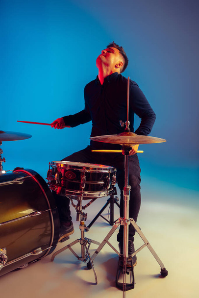 Caucasian male drummer improvising isolated on blue studio background in neon light - Fotó, kép