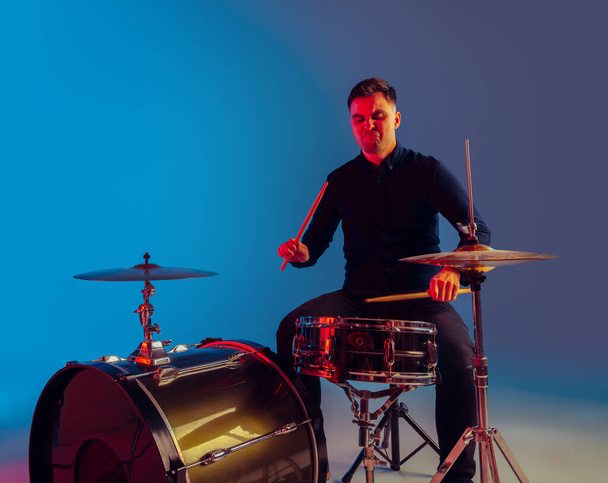 Caucasian male drummer improvising isolated on blue studio background in neon light - Valokuva, kuva