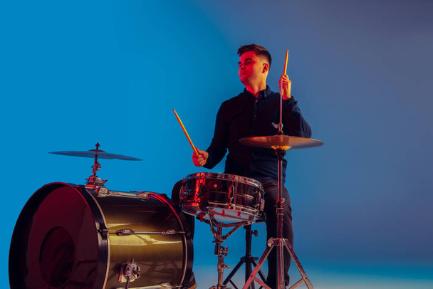 Caucasian male drummer improvising isolated on blue studio background in neon light - Фото, изображение