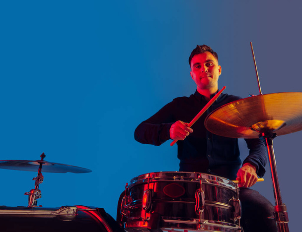 Caucasian male drummer improvising isolated on blue studio background in neon light - Fotoğraf, Görsel