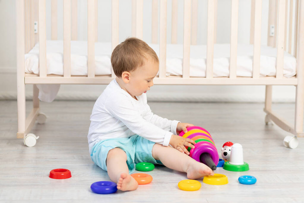 kind spelen in de buurt van de wieg, baby jongen 2 jaar oud zitten met speelgoed, vroege ontwikkeling. - Foto, afbeelding