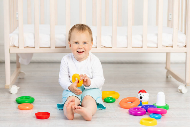 niño jugando cerca de la cuna, bebé niño de 2 años sentado con juguetes, desarrollo temprano
. - Foto, Imagen