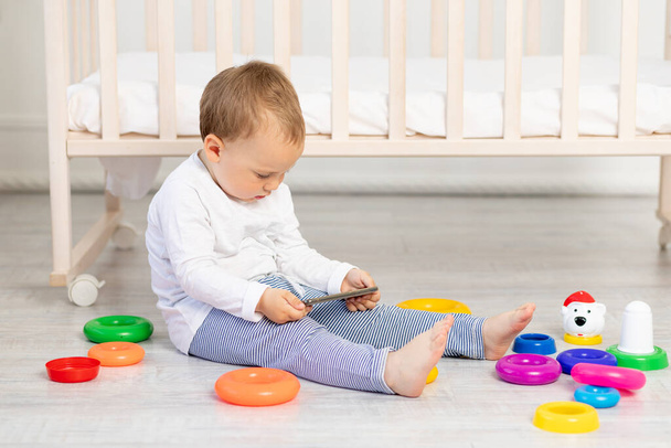 niño jugando cerca de la cuna, bebé niño de 2 años sentado con juguetes, desarrollo temprano
. - Foto, Imagen