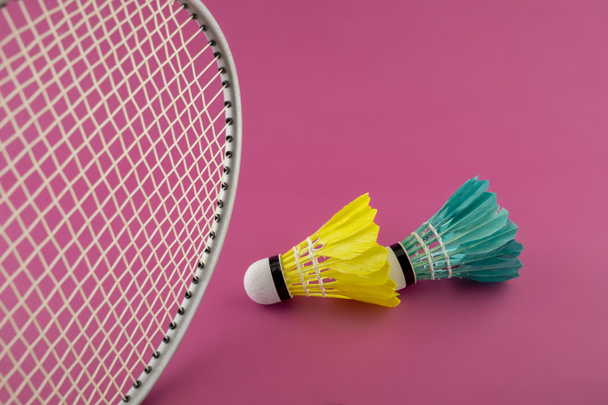 Badminton rackets and colorful feathered shuttlecocks in green and yellow on a pink background - Photo, Image