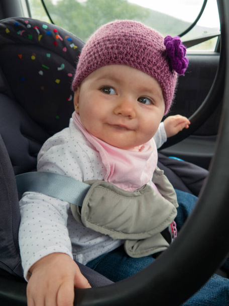 Happy cute little baby. She is on her car seat wearing a hat and looking back. - Photo, Image