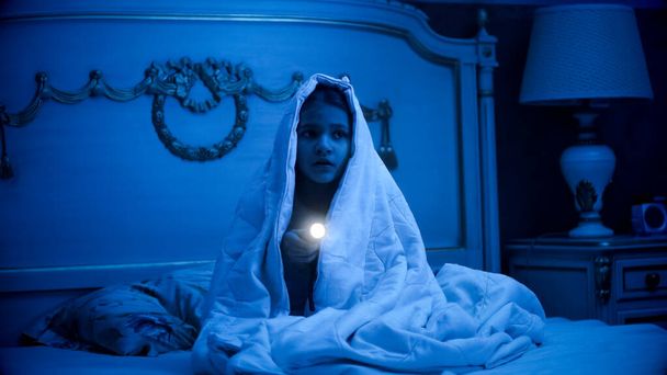 Portrait of afraid of nightmares little girl hiding under blanket in bed - Foto, immagini